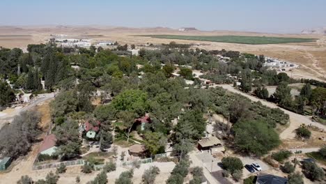 Aerial-backwards-panoramic-drone-shot-of-kibbutz-Sde-Boker,-filled-with-trees,-bushes,-fields,-trails,-buildings-and-houses
