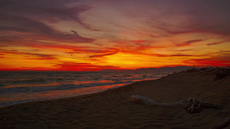 Beautiful-4K-UHD-Cinemagraph-seamless-video-loop-of-of-the-sunset-seen-from-a-romantic-sandy-beach-with-driftwood-and-waves-at-the-Italian-Mediterranean-seaside-with-red-and-orange-clouds-in-the-sky