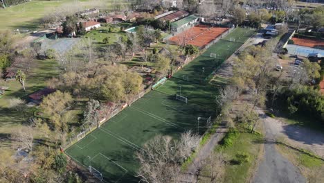 Aerial-view-of-several-soccer-fields-with-some-people-playing-inside-them,-located-between-trees-in-the-facilities-of-a-private-club