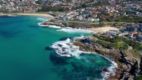 Luftaufnahme-Von-Wellen,-Die-Im-Sommer-Am-Strand-Von-Tamarama-Und-Bronte-Mit-Küstenvorort-In-Sydney,-NSW,-Australien-Zusammenbrechen