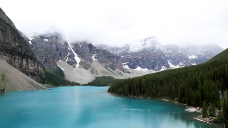 Turquoise-Moraine-Lake-in-Banff-National-Park,-Alberta-Canada-on-a-cloudy-overcast-day-with-tourists-canoeing-and-kayaking-on-blue-lake