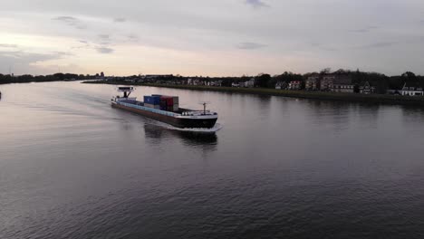 Acadia-Frachtschiff,-Beladen-Mit-Intermodalen-Containern,-Segelt-In-Der-Abenddämmerung-über-Den-Fluss-In-Den-Niederlanden