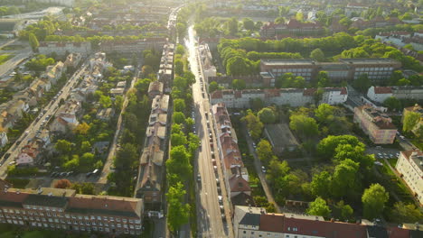 Gdansk-City-Residential-Area-in-Summer-at-golden-hour,-Vehicles-Parked-On-Roadside-Along-with-Buildings,-Blocks-of-Houses-with-Green-Parks---aerial-view,-back-flying-motion