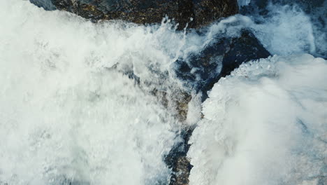 strong-water-flow-in-frozen-river-between-big-stones,-close-up,-slow-motion