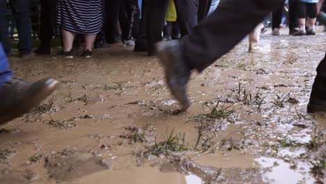 Peoples-legs-seen-walking-through-muddy-puddles-in-wet-footwear-after-downpour-of-rain-at-summer-festival