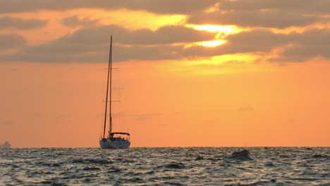 Einsames-Segelboot-Verankert-Auf-Offener-See-Mit-Orangefarbenem-Horizont-Von-Der-Abendsonne-Im-Hintergrund,-Vollbild-Zeitlupe