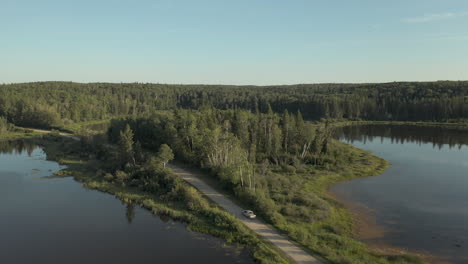 Truck-And-Car-Driving-On-The-Road-Through-Lakes-In-Boreal-Forest,-Saskatchewan,-Canada
