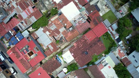 Drone-footage-of-streets-and-colorful-red-rooftops-of-Antigua,-Guatemala-during-the-day-with-normal-car-and-motorcycle-traffic-showing-buildings-and-green-tree-tops