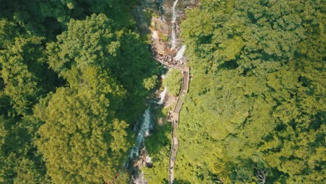 Epic-drone-footage-of-people-walking-on-a-footbridge-at-the-base-of-Amicalola-Falls,-a-729-foot-waterfall