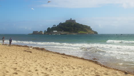 St-Michaels-Mount-with-People-Walking-on-Beach-on-a-Beautiful-Summer-Day,-wide-shot