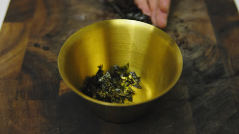 Chef-putting-fresh-seaweed-inside-golden-bowl-during-cooking-meal,slow-motion