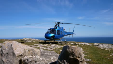 Private-tour-helicopter-on-mountain-cliff-summit-overlooking-blue-ocean-landscape-preparing-for-takeoff-slow-right