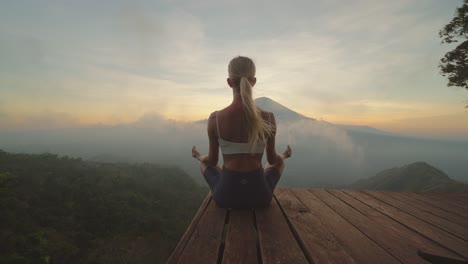 Fit-woman-in-sportswear-meditating-on-platform-with-view-of-Mount-Agung,-sunset
