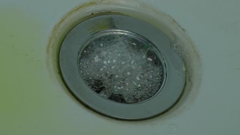 Soap-Foam-And-Water-Swirling-In-Sink-Drain-Hole---high-angle,-close-up