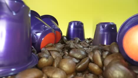 Dolly-shot-of-falling-roasted-coffee-beans-in-slow-motion-surrounded-by-coffee-capsule