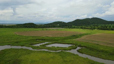 Aerial-reverse-footage-revealing-hills,-lake,-farmlands,-and-a-marshy-land-below-then-the-railroad,-Muak-Klek,-Saraburi,-Thailand