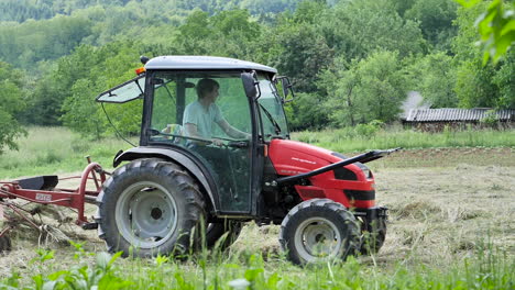 Young-farmer-driving-a-tractor-and-turning-the-hay-on-local-meadow