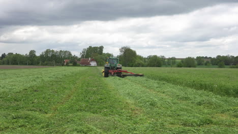 Traktor-Mäht-Gras-Auf-Grünem-Landwirtschaftlichen-Feld-Unter-Dramatischem-Himmel,-Weite-Sicht-In-Zeitlupe