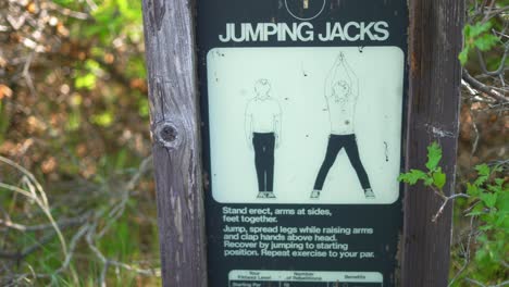 Old-worm-jumping-jacks-instruction-demo-sign-posted-on-wood-frame-a-long-time-ago-outside-at-workout-fitness-hiking-trail-public-national-park