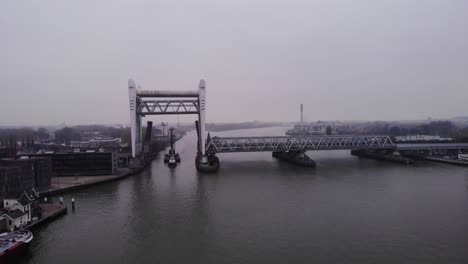 En-Avant-9-Tug-Vessel-Transporting-Heavy-Equipment,-Passing-By-The-Opened-Dordrecht-Railway-Bridge-In-Netherlands