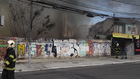 Fireman-climbs-ladder-to-access-smoky-urban-fire-behind-concrete-wall,-on-Tereza-Cristina-avenue,-Ipiranga-district