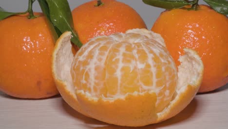 Close-up-shot-rotating-around-a-Kitchen-table-to-reveal-a-half-peeled-ripe-Mandarin-orange,-a-sweet-tasting-citrus-fruit-which-is-easy-to-peel-for-a-healthy-organic-snack