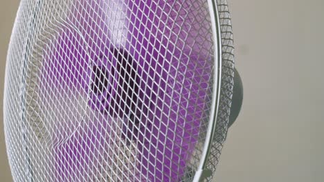 Home-appliance-oscillating-electric-fan-rotating-purple-plastic-blades-circulating-air-in-room-close-up