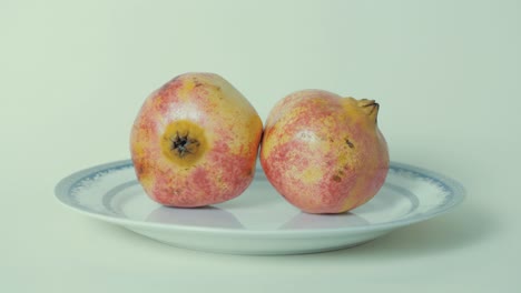 Ripe-pomegranate-fruit-on-plate-against-white-background