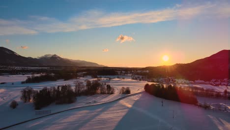 Drone-shot-of-mountains,-fields,-and-landscape-in-winter-at-golden-hour,-sunrise-with-snow,-flying-over-hills-and-fields-with-vibrant-colors