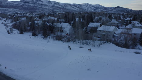 Drohnenansicht,-Die-Im-Winter-Bei-Sonnenuntergang-über-Menschen-Fliegt,-Die-Durch-Dicke-Schneeschichten-Am-Straßenrand-Um-Park-City-In-Utah-Nach-Hause-Gehen