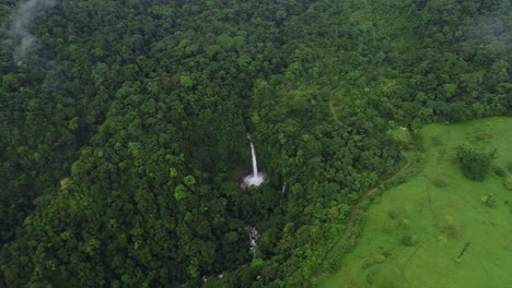 Aerial-over-dense-tropical-rain-forest-with-tall-waterfall-coming-from-cliff,-4K