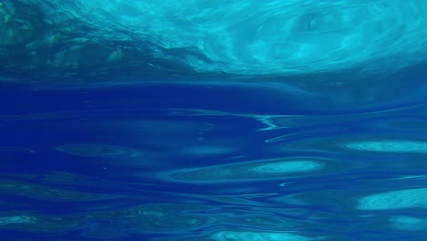 Echte-Unterwasseransicht-Der-Türkisfarbenen-Meeresoberfläche,-Wellenförmig-Und-Lichtstrahlen-Reflektierend