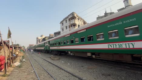 Grüner-Intercity-Zug,-Der-Neben-Gleisen-In-Dhaka,-Bangladesch,-An-Städtischen-Slumhäusern-Vorbeifährt