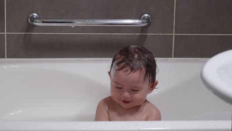 Adorable-Asian-Toddler-Clapping-Hands-While-Bathing-In-A-Baby-Bathtub-In-The-Bathroom