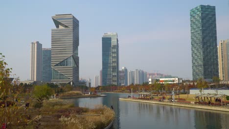A-view-of-the-man-made-lake-in-Incheon's-Central-Park-in-South-Korea,-the-G-Tower,-and-a-view-of-the-city-skyline-in-autumn