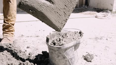 Worker-manually-scoops-cement-into-bucket-with-spade-on-construction-site