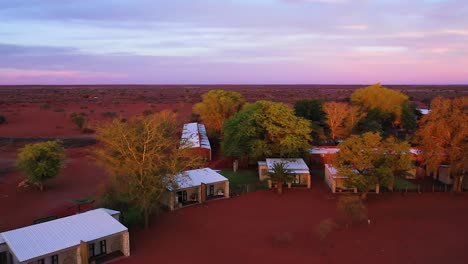 Drone-flying-backwards-over-of-a-lodge-in-the-middle-of-the-African-desert-with-many-small-apartments-and-green-grounds-in-sunset