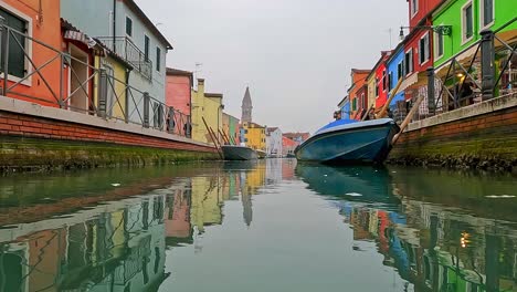 Panning-water-surface-pov-view-of-Burano-colorful-houses-and-canal-with-docked-boats,-Italy