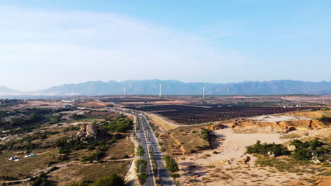 Wind-and-solar-panel-farm-in-Vietnam-landscape-near-highway-road,-aerial-view