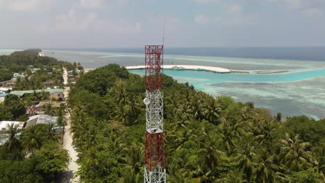 A-high-cell-tower-stands-in-a-town-on-the-ocean-surrounded-by-green-trees-against-a-beautiful-sky