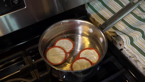 Placing-canning-jar-lids-in-hot-water-on-the-stove-to-heat-up-the-seals---isolated