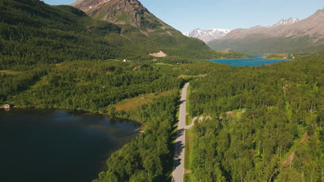 Vista-Aérea-De-Una-Carretera-Rural-Cerca-De-La-Orilla-Del-Lago-Con-Colinas-Y-Picos-Montañosos-Cerca-De-Tromso,-Norte-De-Noruega
