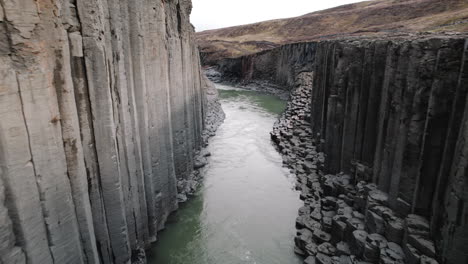Aerial-dolly-past-basalt-columns-of-Studlagil-Canyon,-Iceland,-above-river