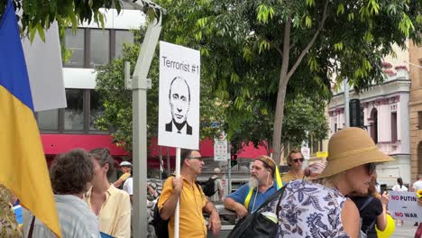 Eine-Gruppe-Von-Menschen-Mit-Unterschiedlichem-Hintergrund,-Die-Sich-Friedlich-Am-Brisbane-Square-Versammelt-Hat,-Drückt-öffentlich-Ihren-Zorn-Aus,-Indem-Sie-Ein-Plakat-Hochhält,-Das-Wladimir-Putin-Als-Den-Terroristen-Nummer-Eins-Zeigt