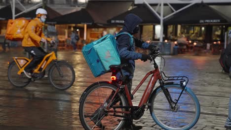 Deliveroo-Rider-Getting-on-his-Electric-Bike-and-Rides-on-the-City-Center-Street-To-Deliver-Orders-for-Clients-and-Customers---Following-courier-shot