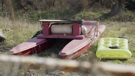 Abandoned-Red-catamaran-left-on-the-side-with-a-yellow-air-mattress-next-to-it-in-the-nature-of-Sabaudia-in-Italy-on-a-sunny-day