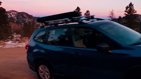 Stunning-tracking-shot-of-a-blue-SUV-driving-along-a-snowy-dirt-mountain-road-during-sunset
