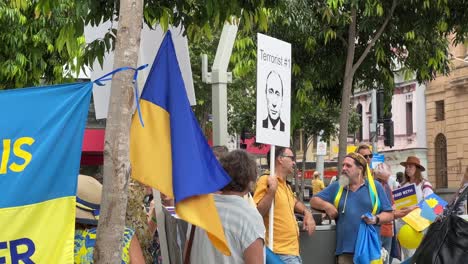 Große-Gruppe-Von-Menschen-Unterschiedlicher-Nationalität,-Die-Ukrainische-Flagge-Schwenken-Und-Ein-Schild-Hochhalten,-Das-Darauf-Hinweist,-Dass-Wladimir-Putin-Während-Einer-Friedlichen-Demonstration-Auf-Dem-Brisbane-Square,-Australien,-Ein-Terrorist-Ist
