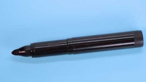 Schwarzer-Markierungsstift,-Der-Sich-Auf-Blauem-Oberflächenhintergrund-Dreht,-Makroaufnahme-Nahaufnahme-Detail