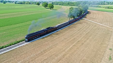 Aerial-View-of-an-Antique-Steam-Engine-and-Passenger-Coaches-Traveling-Along-Countryside-Blowing-Smoke-and-Drone-Traveling-in-Front-of-It,-on-a-Sunny-Summer-Day